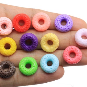 Op de afbeelding: Assortiment van kleurrijke donutvormige kralen met een textuur. De kralen zijn in verschillende kleuren, waaronder roze, rood, paars, geel, groen, blauw, bruin en lichtblauw.