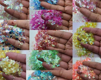 Puede incluir: Surtido de escamas de purpurina iridiscente en varios colores, incluyendo blanco, azul, rosa, verde, amarillo y naranja. La purpurina se muestra en pequeños montones en las palmas de las manos.