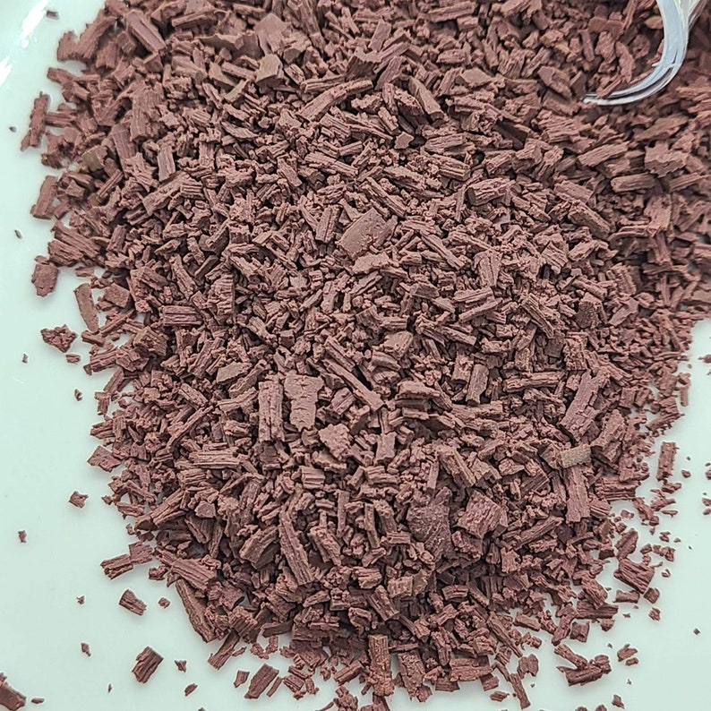 May include: A close-up of a pile of small, dark brown wood chips. The chips are irregularly shaped and have a rough texture.