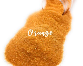 Peut inclure: Gros plan sur un tas de paillettes orange avec un pot en verre transparent qui déverse les paillettes. Le mot "Orange" est écrit en cursive blanche sur les paillettes.