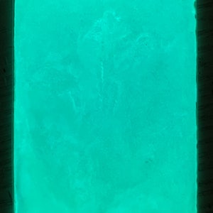 May include: A close-up of a bright green glow-in-the-dark powder. The powder is in a clear plastic bag and is evenly distributed.