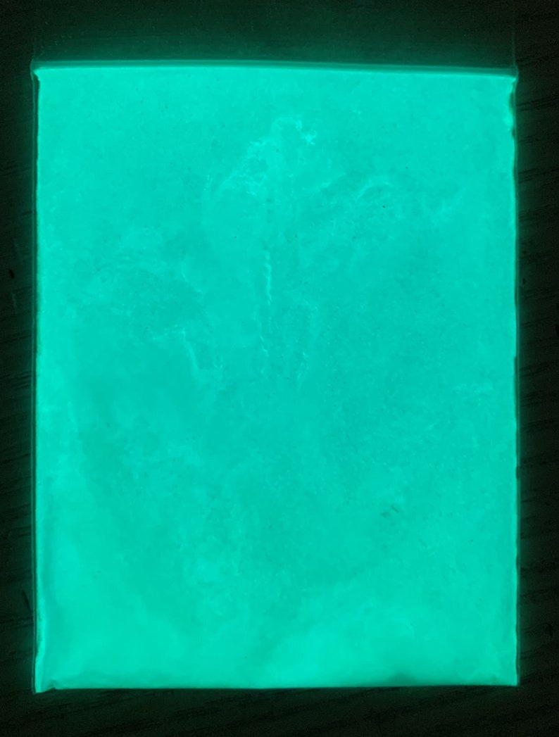 May include: A close-up of a bright green glow-in-the-dark powder. The powder is in a clear plastic bag and is evenly distributed.