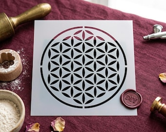 May include: A square white stencil featuring a black geometric flower of life pattern consisting of multiple overlapping circles within a larger circular border. The stencil is flat and displays a repeating symmetrical design of interconnected petals.