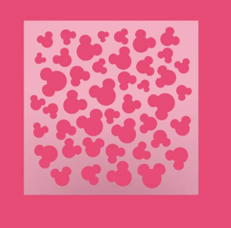 K&ouml;nnte beinhalten: Rosafarbene Schablone mit einem sich wiederholenden Muster von Mickey-Maus-K&ouml;pfen.