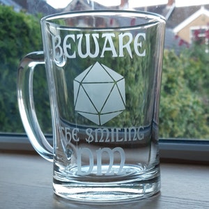 May include: A clear glass mug with a white design that reads "Beware the smiling DM" and features a 20-sided die.