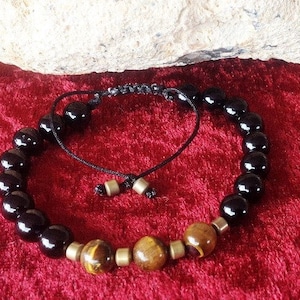 May include: A black and brown beaded bracelet with a black cord closure. The bracelet features round black beads and three round brown beads with gold accents.