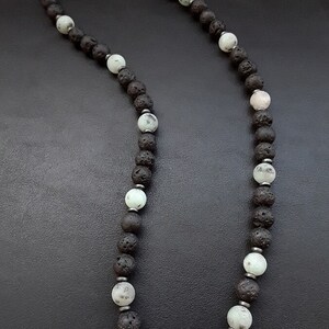 May include: A black and green beaded necklace with a silver clasp. The necklace is made of lava rock and green jasper beads.