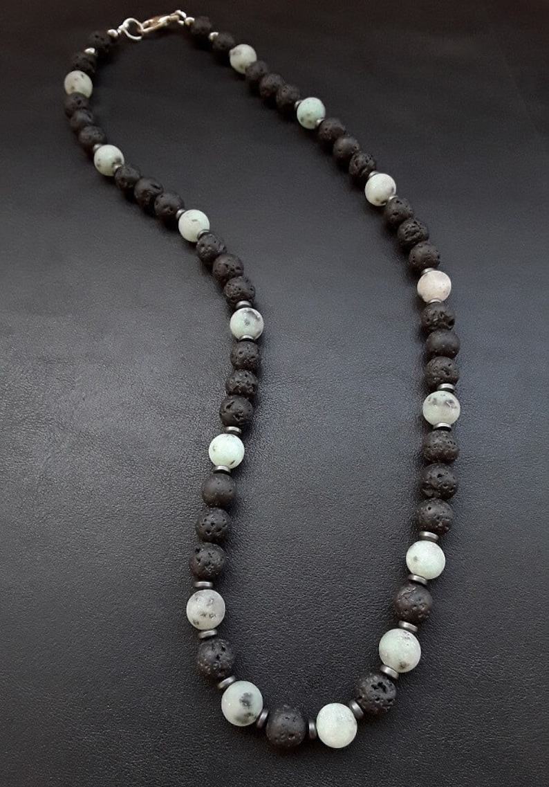 May include: A black and green beaded necklace with a silver clasp. The necklace is made of lava rock and green jasper beads.