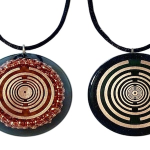 Könnte beinhalten: Zwei schwarze Halsketten mit runden Anhängern, die ein kupferfarbenes Spiralmuster aufweisen. Ein Anhänger hat einen Perlenrand.