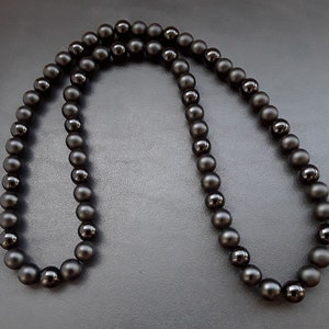 May include: A black beaded necklace made of round, matte black beads. The necklace is approximately 20 inches long and is made of natural stone.