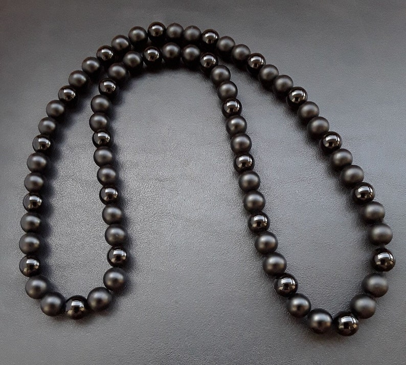 May include: A black beaded necklace made of round, matte black beads. The necklace is approximately 20 inches long and is made of natural stone.
