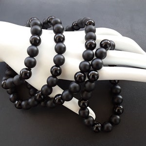 May include: A black beaded necklace made of matte black onyx beads. The necklace is layered and has a long length.