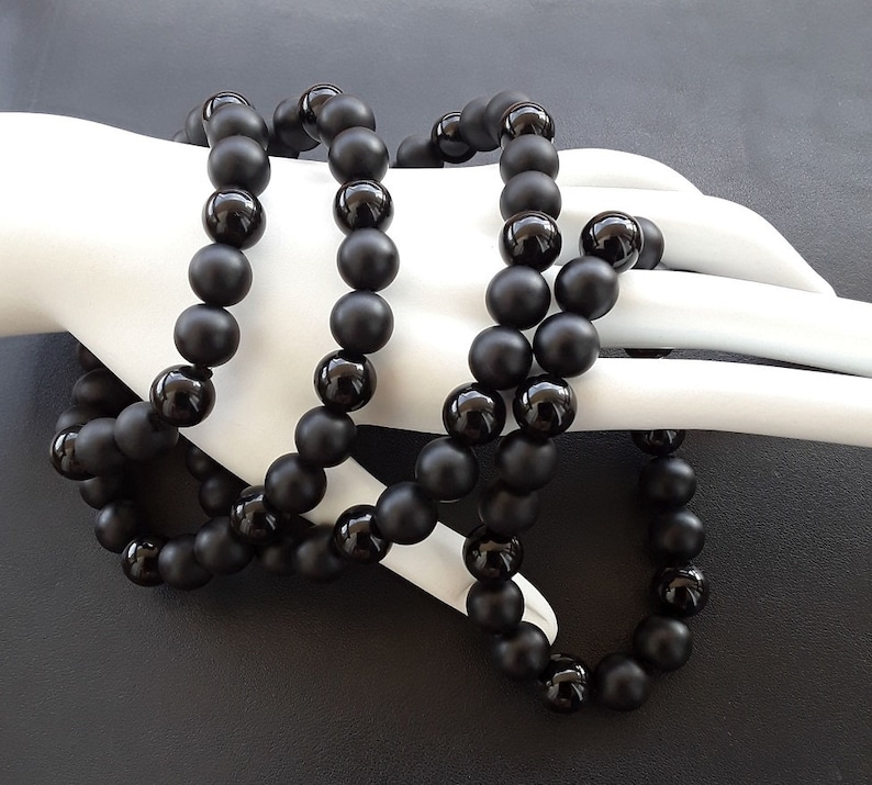 May include: A black beaded necklace made of matte black onyx beads. The necklace is layered and has a long length.