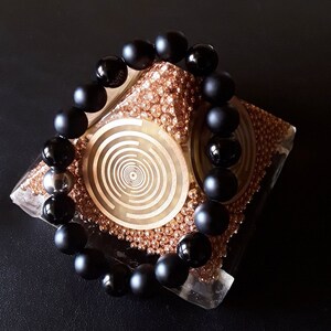 May include: A black onyx beaded bracelet with a matte finish, displayed on a decorative stand with a gold and brown pattern.