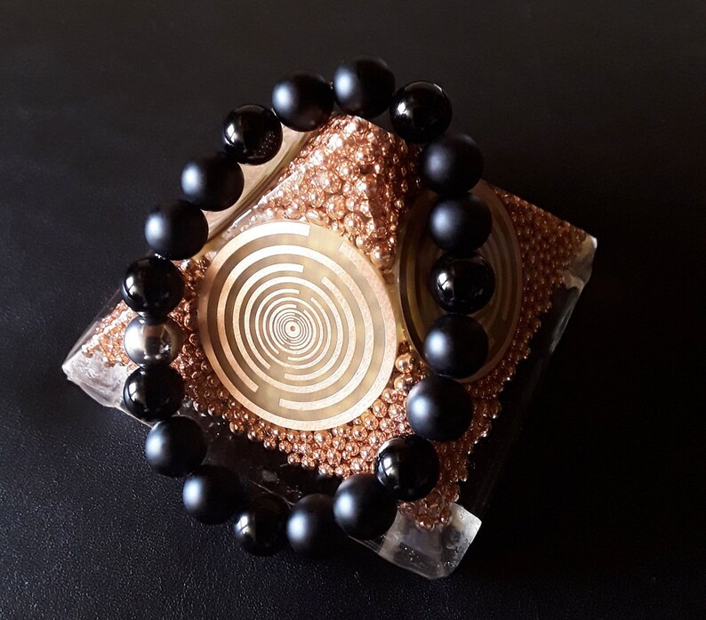 May include: A black onyx beaded bracelet with a matte finish, displayed on a decorative stand with a gold and brown pattern.
