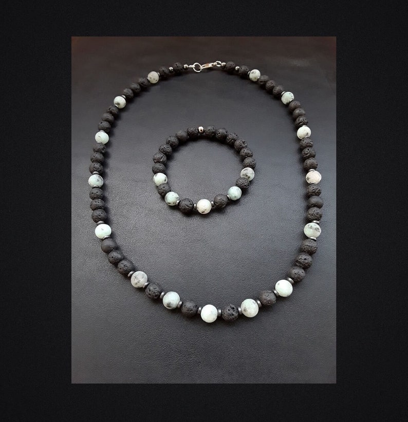 May include: A black and white beaded necklace and bracelet set made of lava rock and white agate. The necklace has a silver clasp.