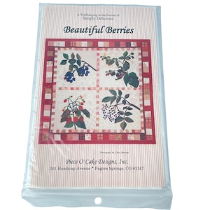 Op de afbeelding: Een pakket met een quiltpatroon getiteld "Beautiful Berries". Het patroon toont een ontwerp van verschillende bessen en bladeren in patchwork-stijl, met een rood-witte rand. De tekst "Piece O' Cake Designs, Inc." is zichtbaar.