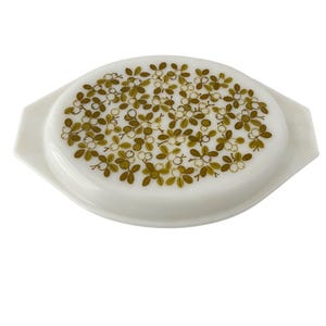 Könnte beinhalten: Ovale, weißes Auflaufform mit Deckel. Der Deckel zeigt ein Muster aus olivgrünen Blättern und weißen Beeren. Die Form hat Griffe und eignet sich zum Servieren von Speisen. Ca. 25 cm lang.