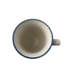 Pu&ograve; includere: Vista dall'alto di una tazza in ceramica bianca con bordo e manico blu. L'interno della tazza &egrave; bianco e il manico &egrave; grigio chiaro. La tazza &egrave; vuota e posta su uno sfondo bianco.