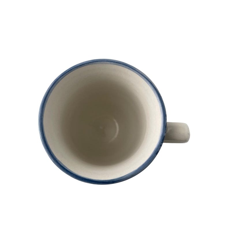 Pu&ograve; includere: Vista dall'alto di una tazza in ceramica bianca con bordo e manico blu. L'interno della tazza &egrave; bianco e il manico &egrave; grigio chiaro. La tazza &egrave; vuota e posta su uno sfondo bianco.