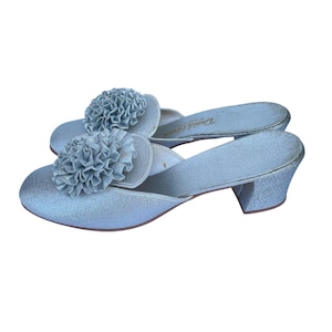 Op de afbeelding: Een paar lichtblauwe satijnen muiltjes met een decoratieve bloem op de wreef. De open schoenen hebben een lage hak en zijn waarschijnlijk vintage. De merknaam "Daniel Green" staat op de binnenzool.