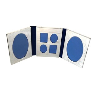 May include: A triptych photo frame with a metallic silver finish and a blue interior lining. The two outer panels feature large oval openings, while the central panel contains four smaller openings consisting of two rectangles and two ovals.