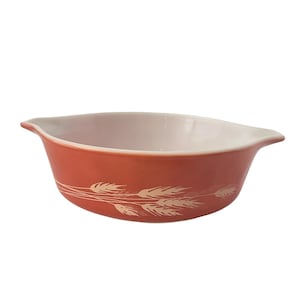 May include: A vintage, orange-red Pyrex bowl with a white interior. The exterior features a wheat pattern in a cream color. The bowl has two handles and is ideal for serving or baking.