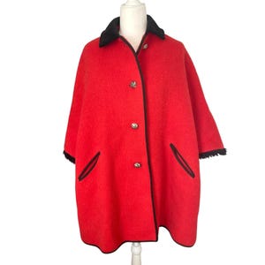 May include: A red wool cape with a black velvet collar and black trim. The cape has a button closure and two pockets.