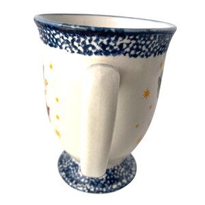 Pu&ograve; includere: Una tazza in ceramica bianca con bordo e base blu maculato. La tazza ha un manico curvo ed &egrave; decorata con illustrazioni e dettagli di stelle gialle. La tazza &egrave; progettata per le bevande.