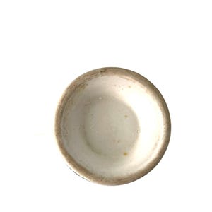 Pu&ograve; includere: Una tazza di ceramica bianca con un interno leggermente strutturato e un bordo marrone scuro. L'interno della tazza presenta alcune piccole macchie gialle. La tazza &egrave; posta su uno sfondo bianco.