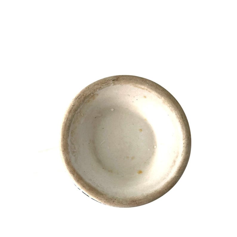 Pu&ograve; includere: Una tazza di ceramica bianca con un interno leggermente strutturato e un bordo marrone scuro. L'interno della tazza presenta alcune piccole macchie gialle. La tazza &egrave; posta su uno sfondo bianco.