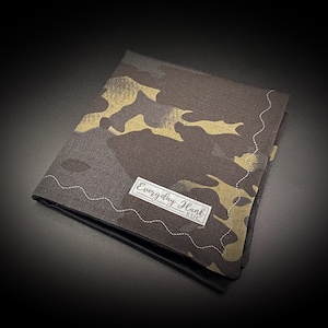 May include: A brown and tan camouflage bandana with a white label that says "Everyday Hank EDC".