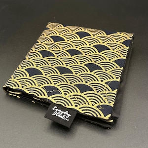 May include: A folded, navy blue wallet with a gold wave pattern. The wallet has a small black tag with the text "Everyday Hank..." in white. The design is a repeating pattern of gold semi-circles on a dark blue background.