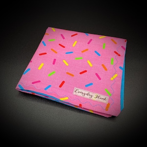 May include: Pink bandana with a blue border and a white label that says "Everyday Hank". The bandana is covered in colorful sprinkles.