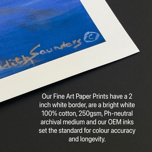 May include: A close-up of a white matted print with a 2-inch white border. The print features a blue sky with a signature that reads "Judith Saunders" in silver lettering. The text below the image reads "Our Fine Art Paper Prints have a 2 inch white border, are a bright white 100% cotton, 250gsm, Ph-neutral archival medium and our OEM inks set the standard for colour accuracy and longevity."