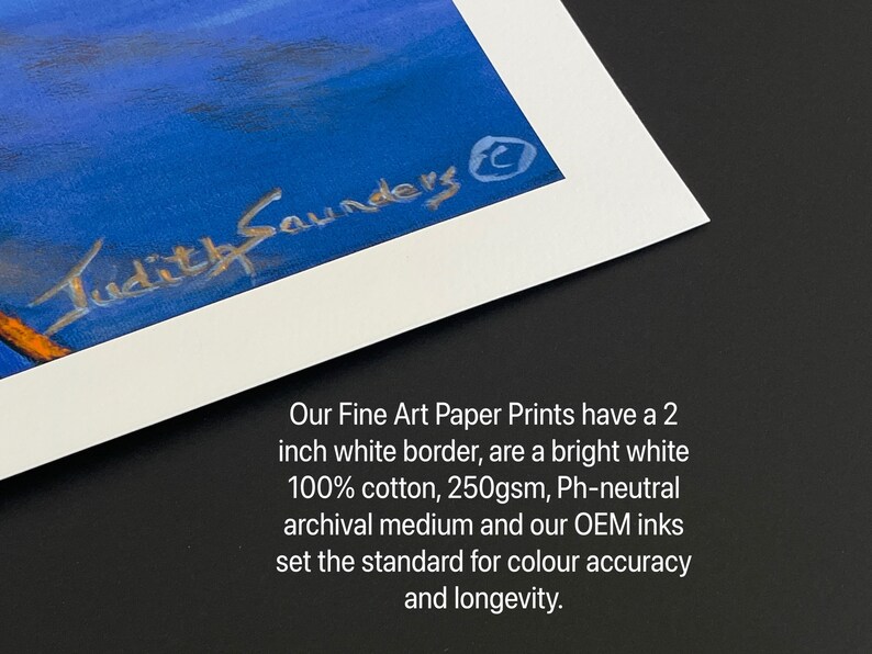 May include: A close-up of a white matted print with a 2-inch white border. The print features a blue sky with a signature that reads "Judith Saunders" in silver lettering. The text below the image reads "Our Fine Art Paper Prints have a 2 inch white border, are a bright white 100% cotton, 250gsm, Ph-neutral archival medium and our OEM inks set the standard for colour accuracy and longevity."