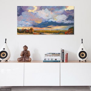 May include: A white, modern, rectangular cabinet with three doors, a wooden top, and two white speakers on the top. A wooden sculpture of a meditating Buddha sits on the top of the cabinet. A stack of books sits on the cabinet top. A painting of a landscape with a cloudy sky hangs on the wall behind the cabinet.