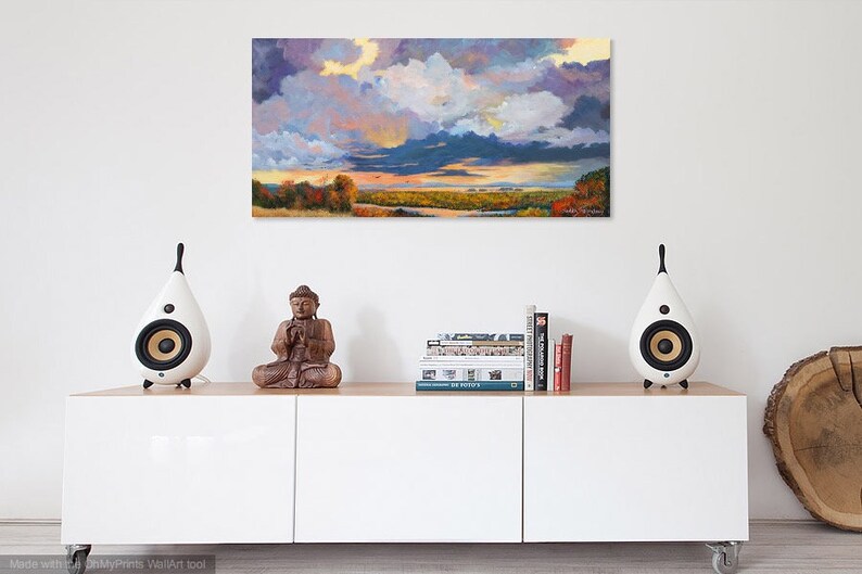 May include: A white, modern, rectangular cabinet with three doors, a wooden top, and two white speakers on the top. A wooden sculpture of a meditating Buddha sits on the top of the cabinet. A stack of books sits on the cabinet top. A painting of a landscape with a cloudy sky hangs on the wall behind the cabinet.