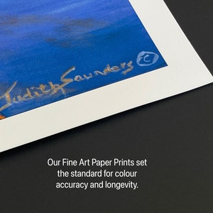 May include: A close-up of a white matted print with a blue and orange painting. The artist's signature, "Judith Saunders", is visible in the bottom right corner of the print. The text "Our Fine Art Paper Prints set the standard for color accuracy and longevity." is printed below the mat.