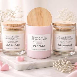May include: Three scented candles with wooden lids and glass jars. The candles are labeled "Love & Linen", "Mi Amour", and "Expresso Love". Each candle has a white label with the text "Flamme & Still Co. FIND YOUR MESSAGE".