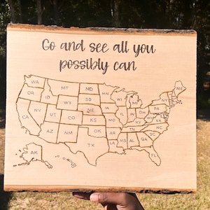 May include: A wooden sign with a map of the United States and the text "Go and see all you possibly can".