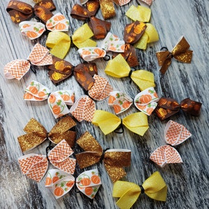 May include: A collection of 20 handmade hair bows in various fall colors and patterns, including orange, brown, yellow, and white. The bows feature pumpkin designs, glitter, and chevron patterns.