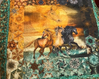 May include: A quilt with a colorful design featuring three horses running through a sunset. The horses are brown, tan, and black. The background is a mix of orange, yellow, and green.
