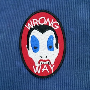 May include: Red and white embroidered patch with a cartoon vampire face and the text "WRONG WAY" in a white circle.