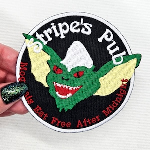 May include: A black and white embroidered patch with a green, yellow, and red creature with large ears. The patch says "Stripe's Pub" and "Moguls Eat Free After Midnight".