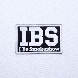 May include: A rectangular embroidered patch featuring a black background with a white border. The letters IBS are stitched in large white block font, with the text I Be Smokeshow embroidered in a smaller white serif font underneath.