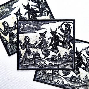 May include: A rectangular fabric patch featuring a black and white woodcut-style illustration of a person standing on a hill, a figure flying on a broomstick, and a horned creature, all set against a landscape with clouds and small buildings.