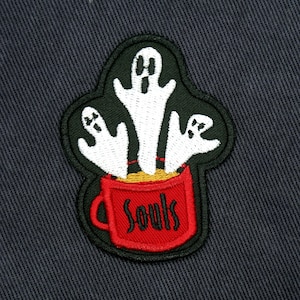 May include: An embroidered patch featuring three white ghosts rising from a red mug with the word "Souls" in black lettering.