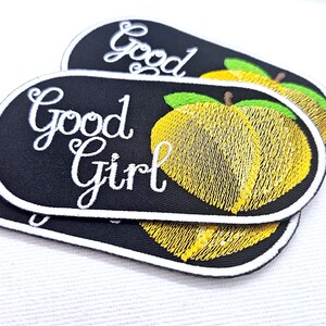 Könnte beinhalten: Ovale, gestickte Aufnäher mit schwarzem Hintergrund, weißem Rand und weißem Schriftzug "Good Girl". Die Aufnäher zeigen ein gelbes Zitronen-Design mit grünen Blättern.