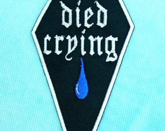 Pode incluir: Patch bordado preto e branco em forma de caixão com o texto "died crying" em branco e uma lágrima azul.